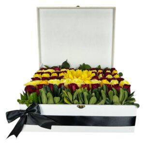 Caja blanca con arreglo de rosas rojas y blancas, girasol al centro y lazo negro.