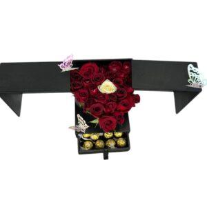Caja negra desplegable con corazón de rosas rojas, rosa blanca central, mariposas decorativas y cajón con chocolates Ferrero Rocher.
