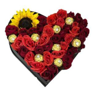 Caja corazón negra con rosas rojas y naranjas, girasol amarillo y chocolates Ferrero Rocher integrados.