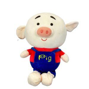 Peluche de cerdito color crema con hocico rosado, camiseta roja y overol azul con la palabra “pig”.